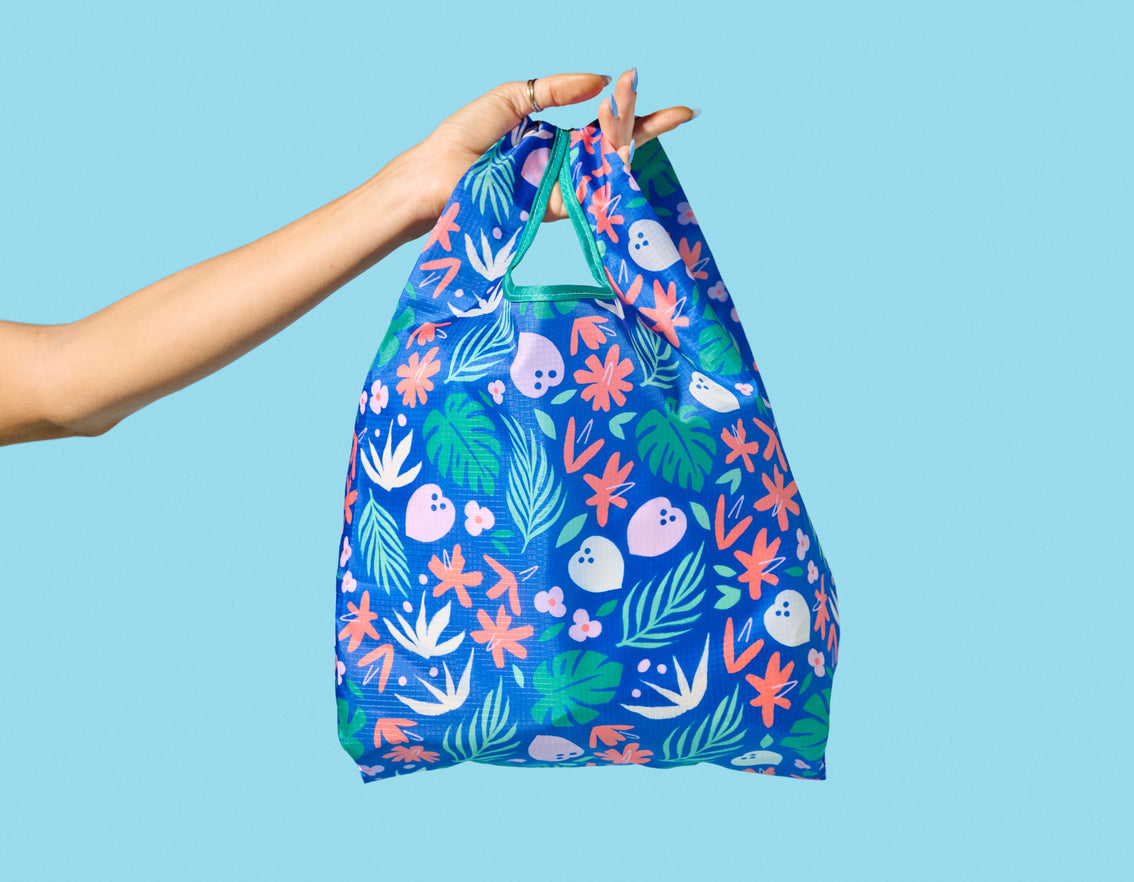 A hand holding a Vita Coco Mini Patterned Foldable Tote shopping bag.