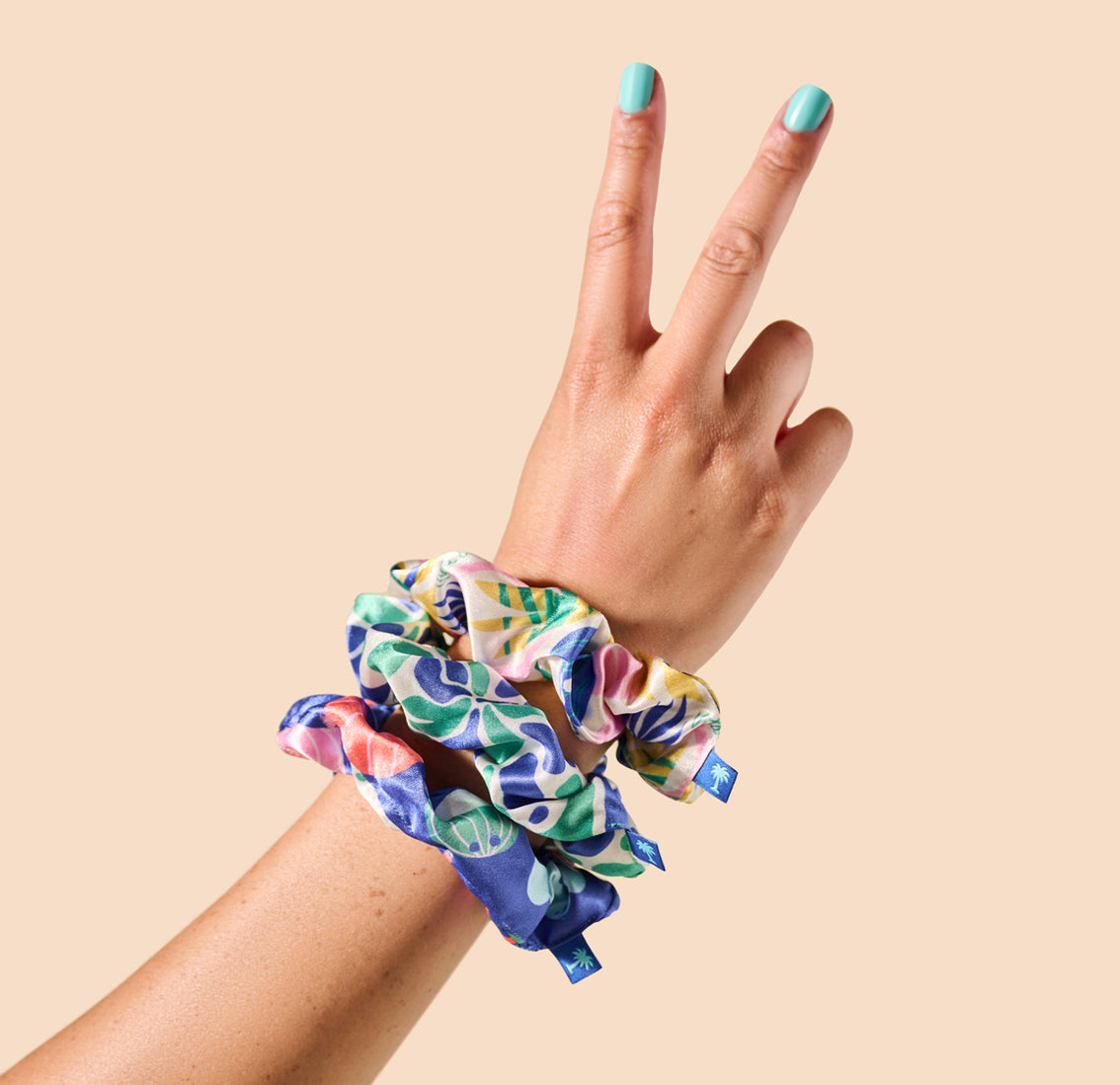 A woman's hand holding a Vita Coco Scrunchie with a peace sign on it, perfect for securing her hair in style.